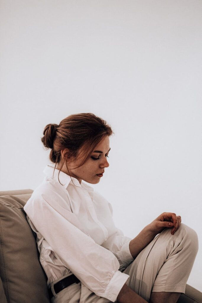 thoughtful woman sitting on sofa against white wall